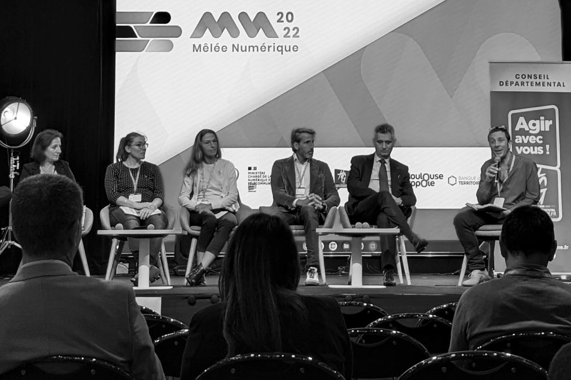 6 personnes sur une scène dont une tient un micro. On voit les logos de la mêlée numérique et du conseil départemental derrière