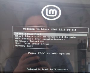 photo d'un écran d'ordinateur avec le menu proposant d'installer Linux Mint. On me voit dans le reflet de l'écran