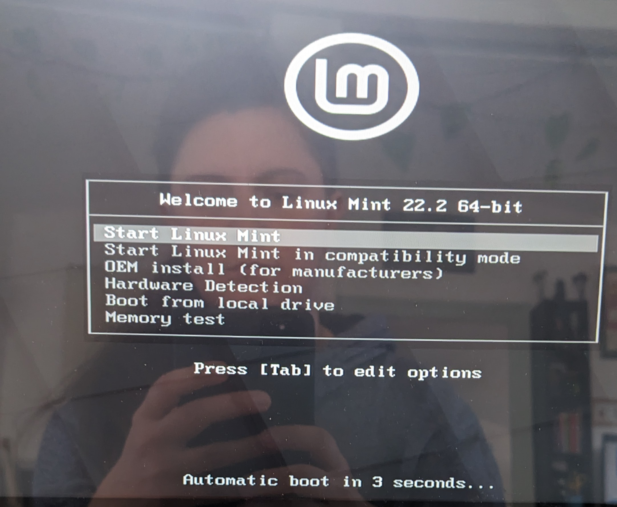 photo d'un écran d'ordinateur avec le menu proposant d'installer Linux Mint. On me voit dans le reflet de l'écran