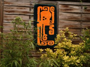 photo d'un tapis tufté avec un motif de poulpe orange, accroché à une palissade derrière des feuillages